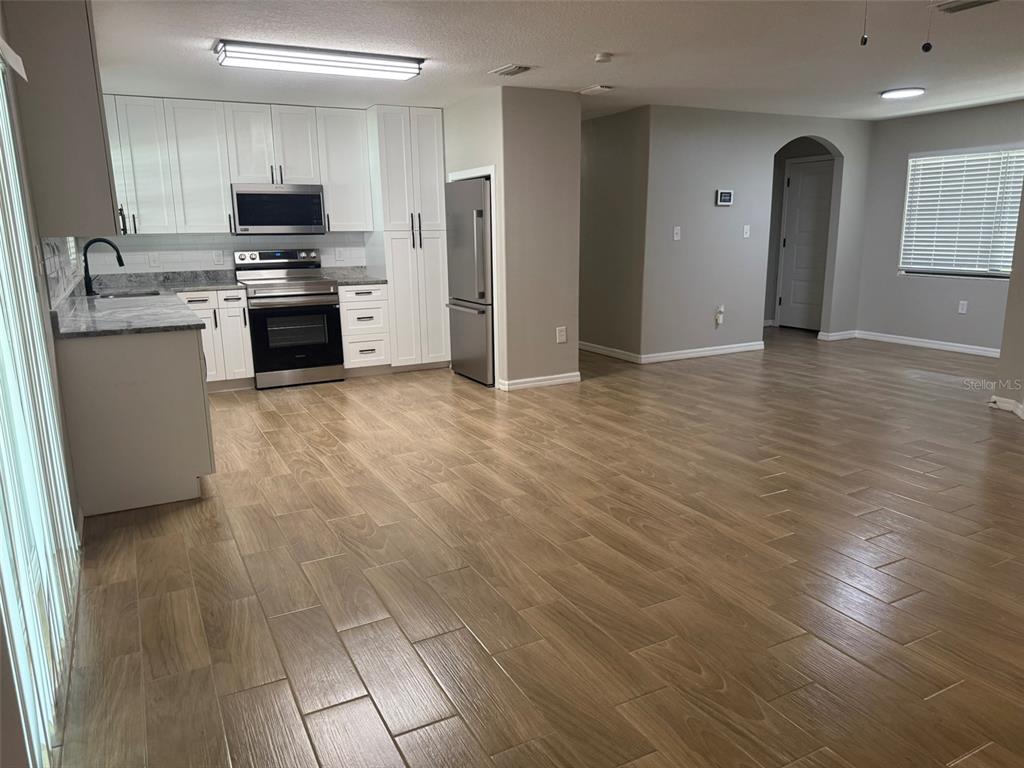 A kitchen with white cabinets and stainless steel appliances opens into a spacious living area — 1008 N BRACEWELL DRIVE, PLANT CITY, FL