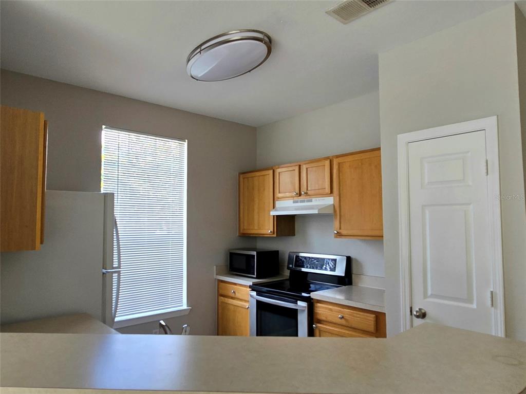 A kitchen features light wood cabinets, a black stove, a microwave, and a window — 9005 LEE VISTA BLVD UNIT 1803, ORLANDO, FL