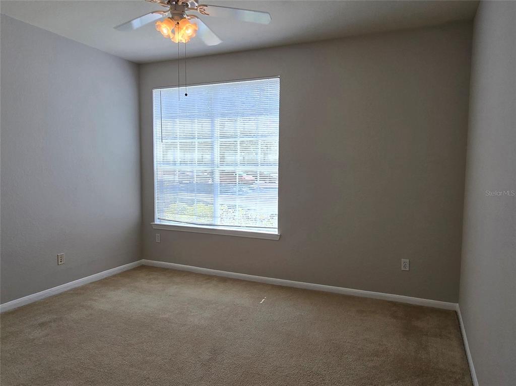 An empty bedroom features beige carpet, light gray walls, a ceiling fan, and a window — 9005 LEE VISTA BLVD UNIT 1803, ORLANDO, FL