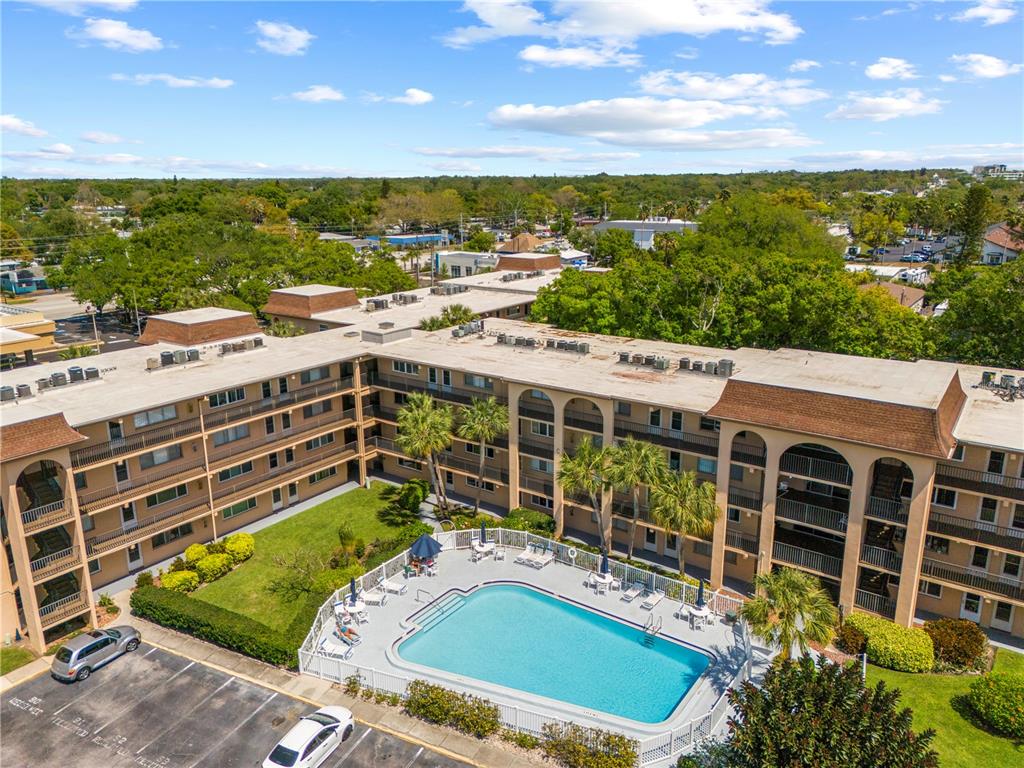 An aerial view shows a multi-story apartment complex with a central swimming pool and parking — 2525 W BAY DRIVE UNIT C21, BELLEAIR BLUFFS, FL