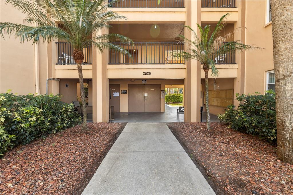 A concrete walkway leads to the ground-level entrance of a multi-story apartment building — 2525 W BAY DRIVE UNIT C21, BELLEAIR BLUFFS, FL