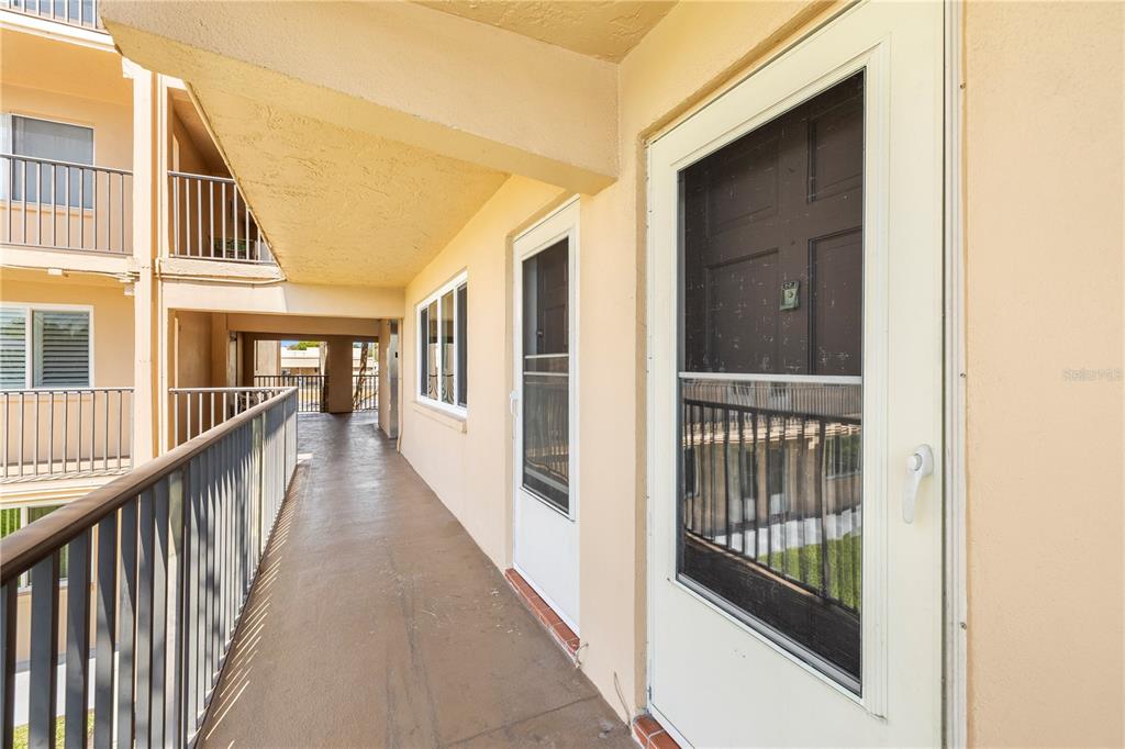 An exterior walkway with a metal railing leads to two apartment doors with screen doors — 2525 W BAY DRIVE UNIT C21, BELLEAIR BLUFFS, FL