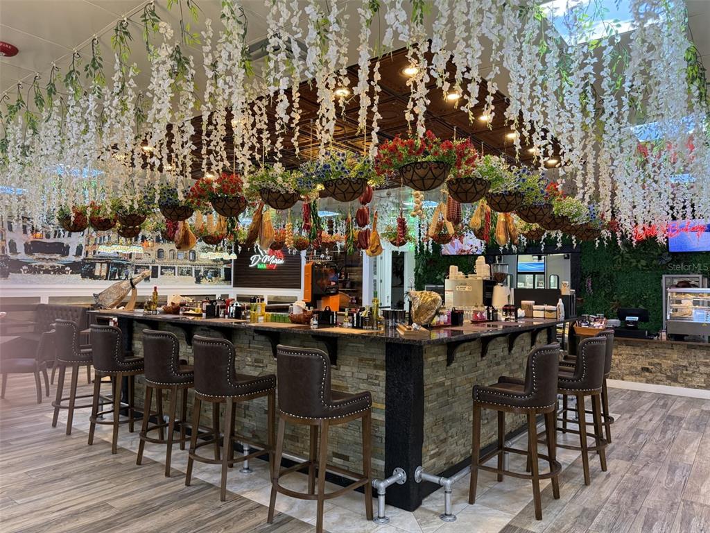 A restaurant bar features stone counters, leather stools, and hanging floral and food decor — 4984 PALM COAST NW PARKWAY, PALM COAST, FL