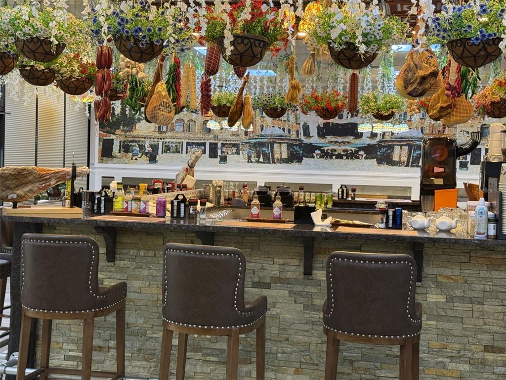A bar area features stone-faced counters, leather stools, and hanging baskets of flowers and meats — 4984 PALM COAST NW PARKWAY, PALM COAST, FL