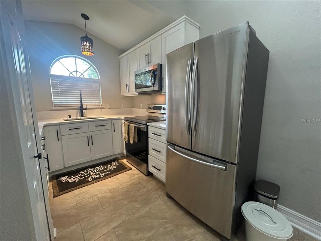 A kitchen features white cabinets, stainless steel appliances, a sink under a window, and tile flooring — 6738 MAGNOLIA POINTE CIRCLE, ORLANDO, FL