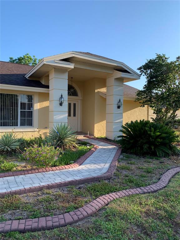 A paved walkway leads to the front entrance of a yellow house with two columns — 8621 ASHBURY DRIVE, HUDSON, FL