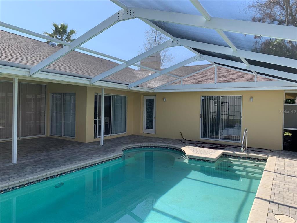 A swimming pool sits on a paved patio enclosed by a white metal screen structure — 8621 ASHBURY DRIVE, HUDSON, FL