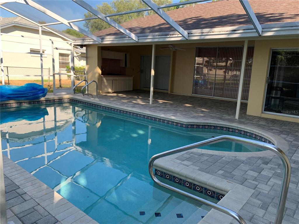 A screened-in patio features a swimming pool with a built-in step and outdoor kitchen — 8621 ASHBURY DRIVE, HUDSON, FL