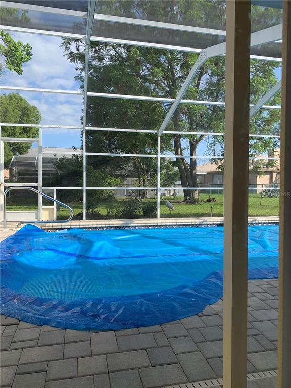 A blue pool cover sits on a swimming pool inside a screened-in patio area — 8621 ASHBURY DRIVE, HUDSON, FL