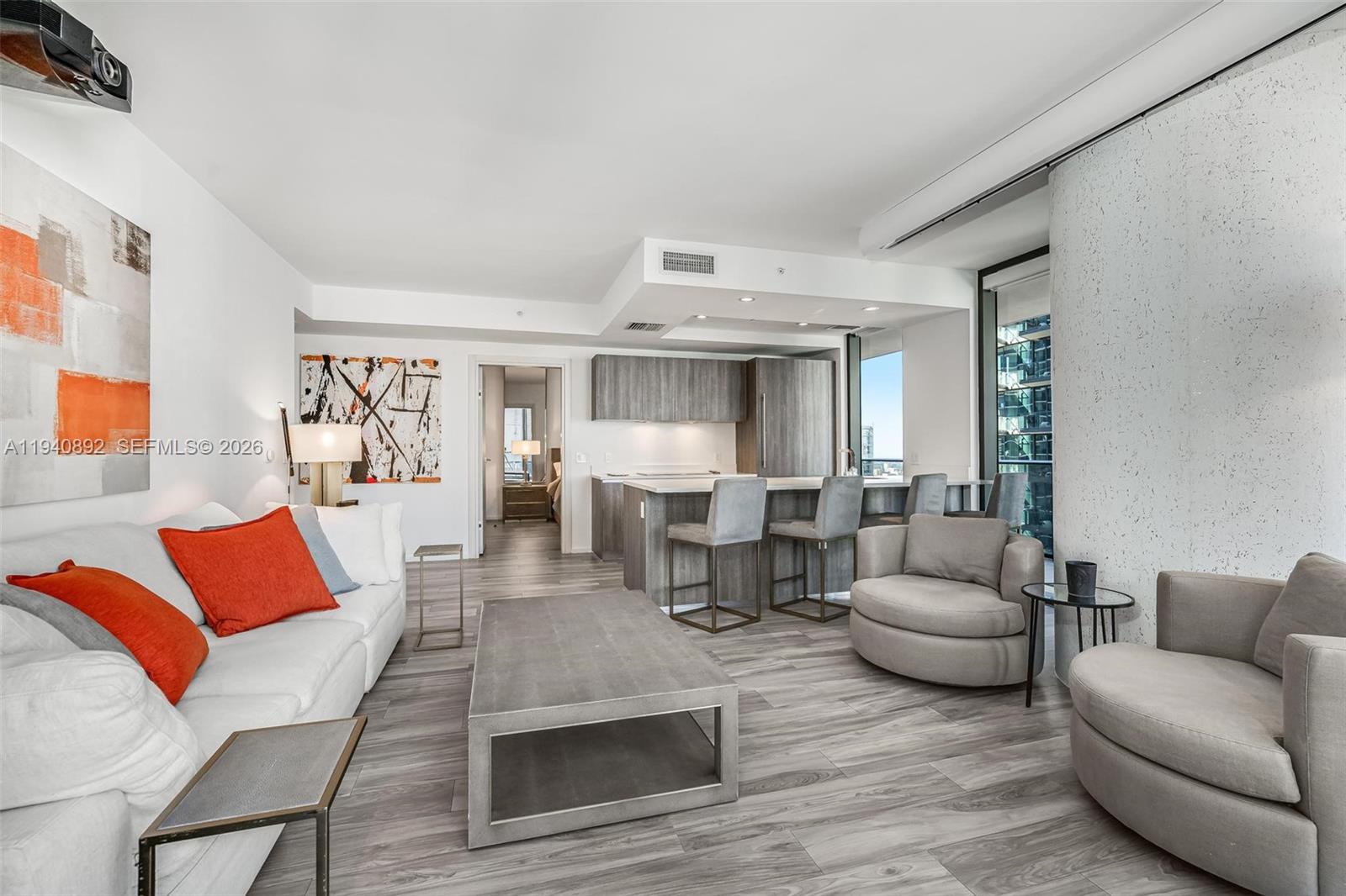 A modern living room features a white sofa, gray armchairs, and an open kitchen area — 801 S Miami Ave # 2905, Miami FL 33130, MIAMI, FL