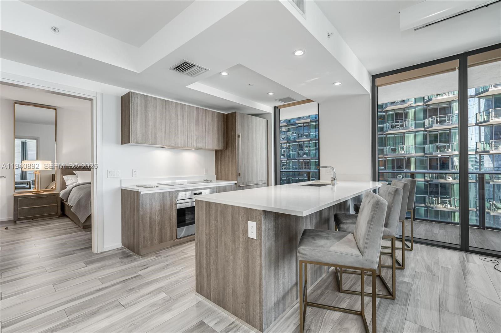 A modern kitchen features wood-grain cabinetry, a white island, and bar stools near a balcony — 801 S Miami Ave # 2905, Miami FL 33130, MIAMI, FL