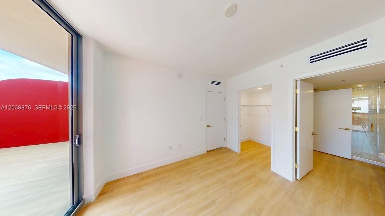 A bright bedroom features light wood-look flooring, a walk-in closet, and access to a balcony — 90 NE 32nd Street # 603, Miami FL 33127, MIAMI, FL