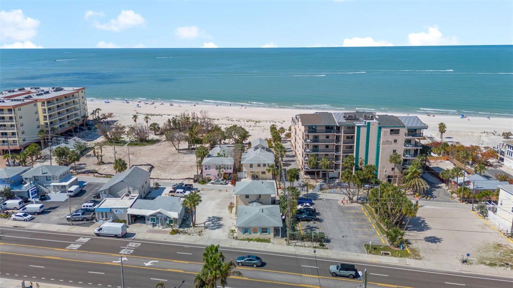 An aerial view shows a coastal area with buildings, a parking lot, and a beach — 13062 GULF BOULEVARD, MADEIRA BEACH, FL