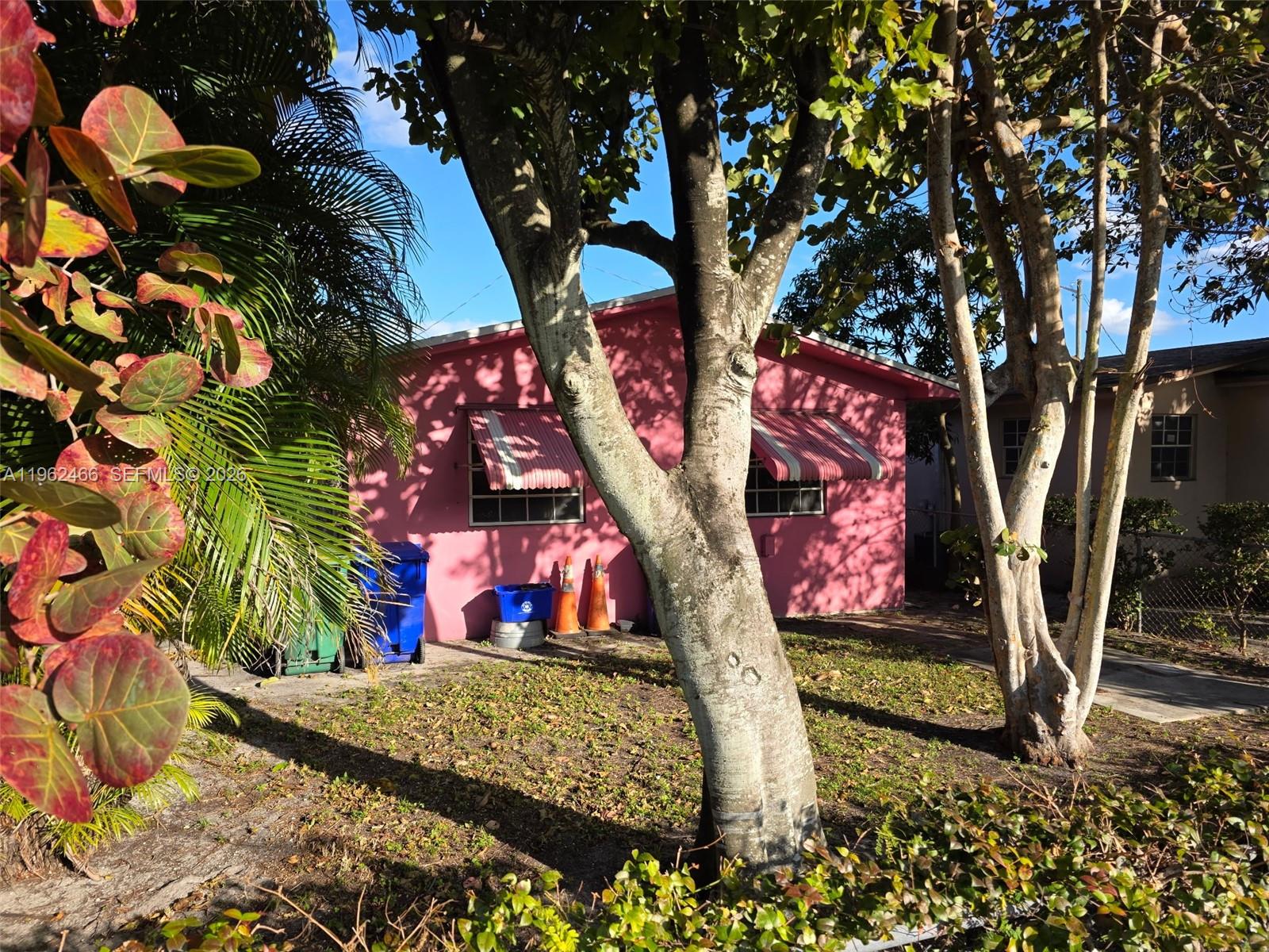 A pink house exterior features two windows with striped awnings and several trees in front — 5132 NW 14th Ave, Miami FL 33142, MIAMI, FL