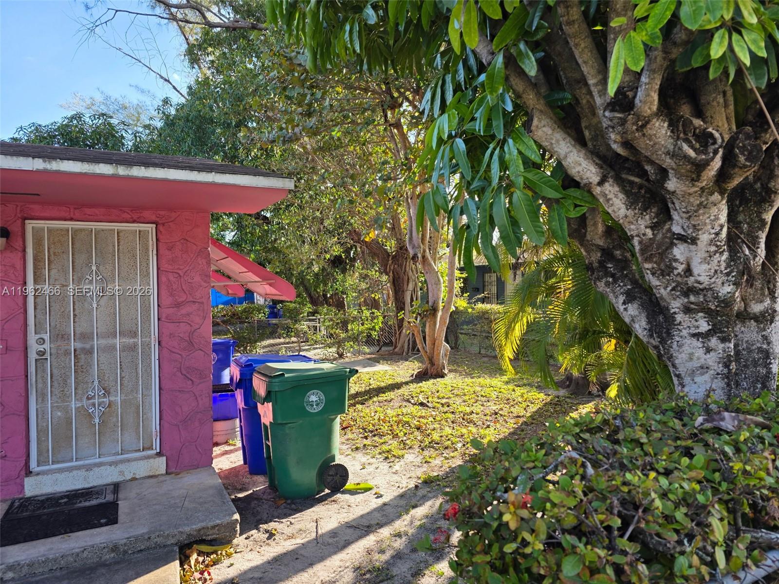 A pink exterior wall with a security door stands beside trash bins and trees — 5132 NW 14th Ave, Miami FL 33142, MIAMI, FL