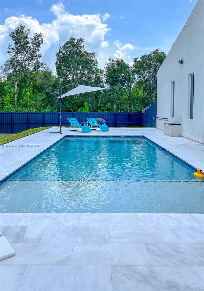 A rectangular swimming pool with a sun shelf sits on a patio beside a white house — 395 Pace Avenue, Lehigh Acres FL 33974, LEHIGH ACRES, FL