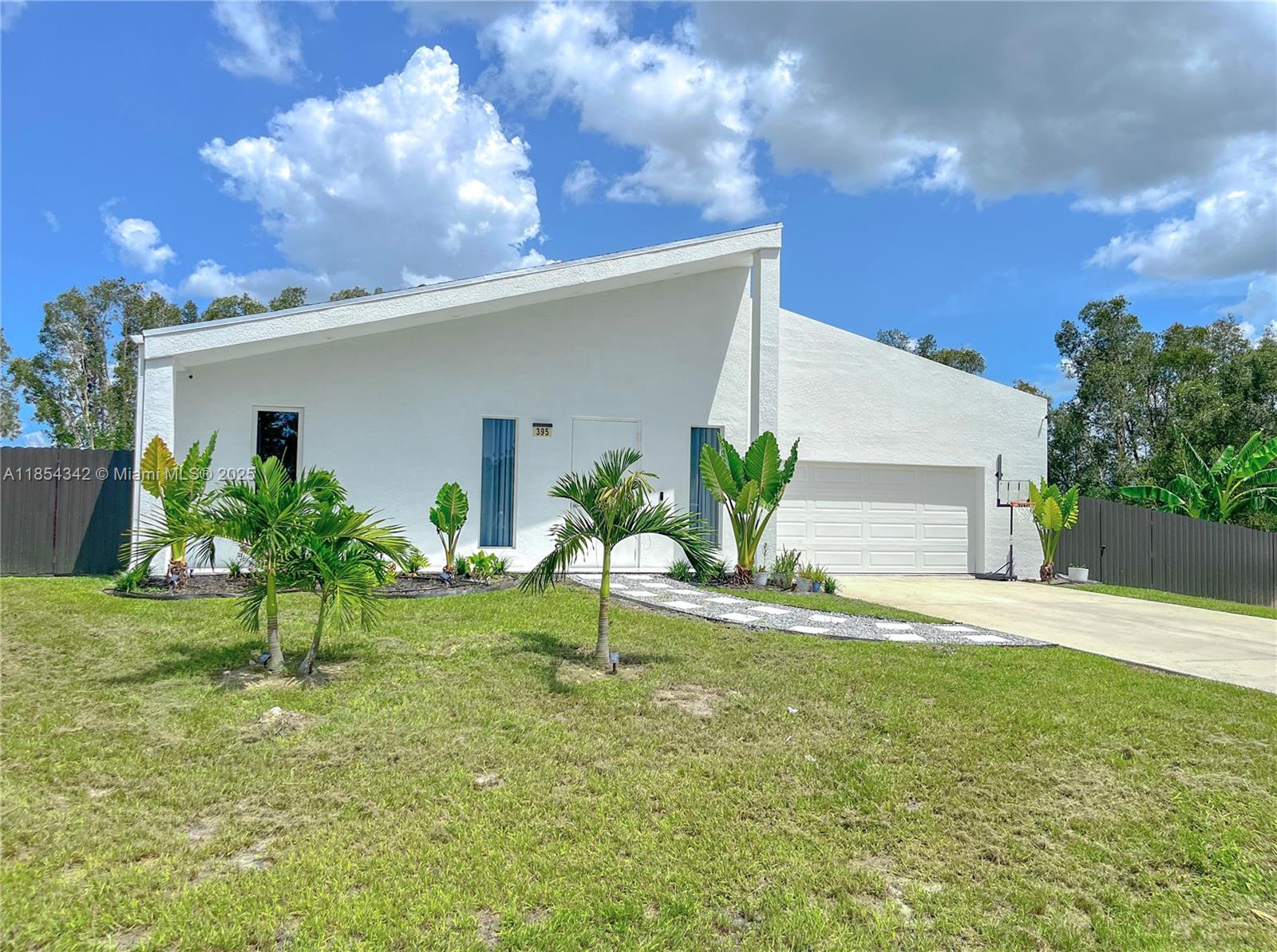 A white, single-story house with a slanted roof, a garage, and palm trees in the yard — 395 Pace Avenue, Lehigh Acres FL 33974, LEHIGH ACRES, FL