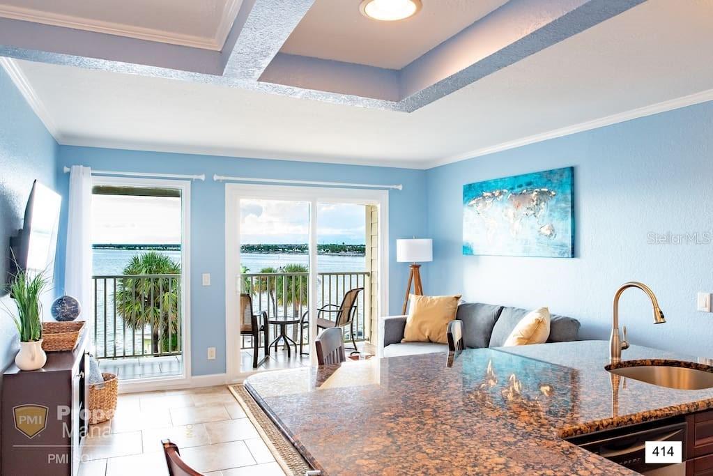 A kitchen island with granite countertops overlooks a living area with a balcony and water view — 2506 N ROCKY POINT DRIVE UNIT 414, TAMPA, FL