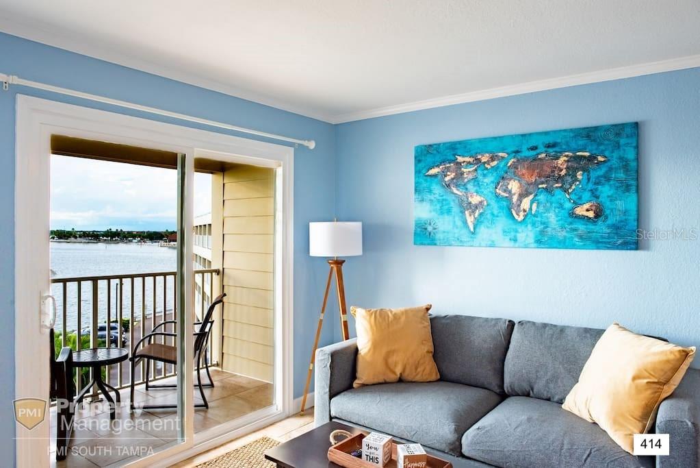 A living room with a gray sofa, world map art, and a balcony overlooking water — 2506 N ROCKY POINT DRIVE UNIT 414, TAMPA, FL