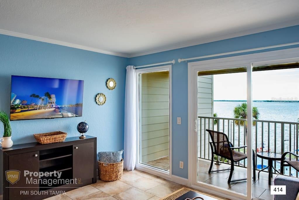 A living room with blue walls, a television, and a balcony overlooking the water — 2506 N ROCKY POINT DRIVE UNIT 414, TAMPA, FL