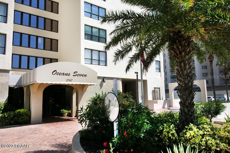 The exterior of the Oceans Seven building features a covered entrance and a palm tree — 2947 S ATLANTIC AVENUE UNIT 606, DAYTONA BEACH, FL