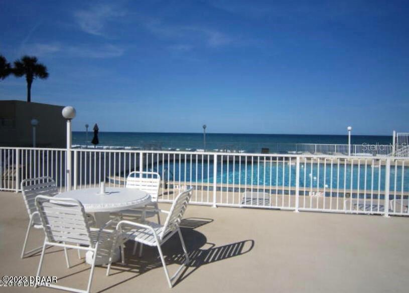 A patio with a white table and chairs overlooks a swimming pool and the ocean — 2947 S ATLANTIC AVENUE UNIT 606, DAYTONA BEACH, FL