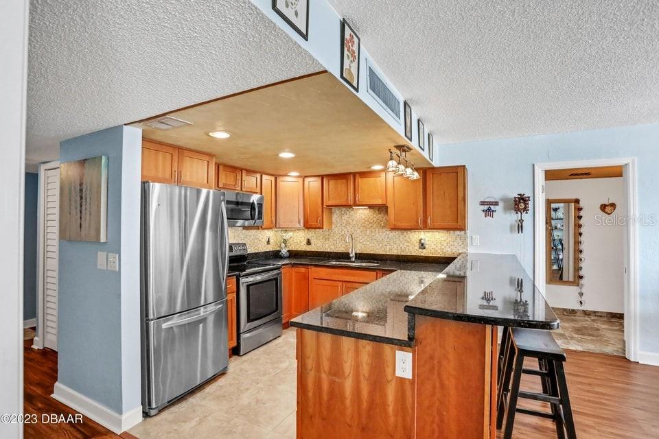 A kitchen features wood cabinets, stainless steel appliances, and a granite-topped breakfast bar — 2947 S ATLANTIC AVENUE UNIT 606, DAYTONA BEACH, FL
