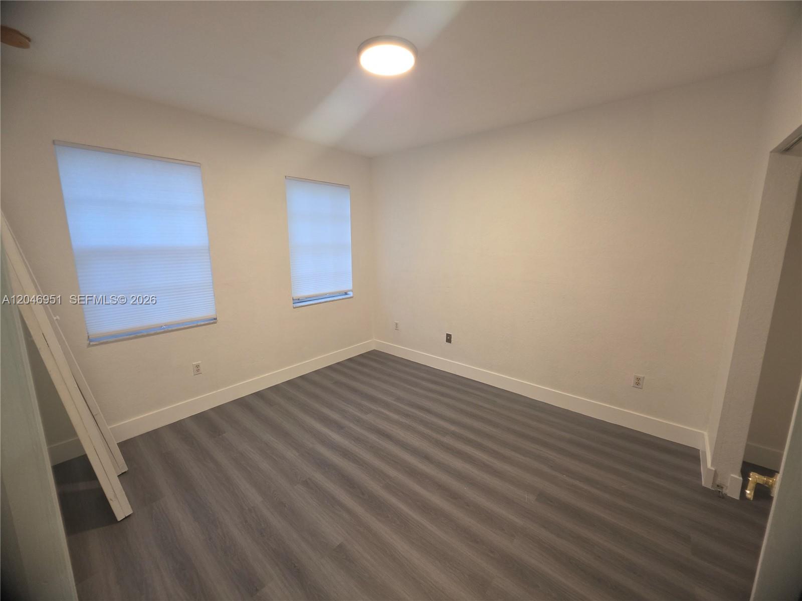 An empty room features white walls, gray wood-look flooring, and two windows with blinds — 2532 SW 85th Ter # 102, Miramar FL 33025, MIRAMAR, FL