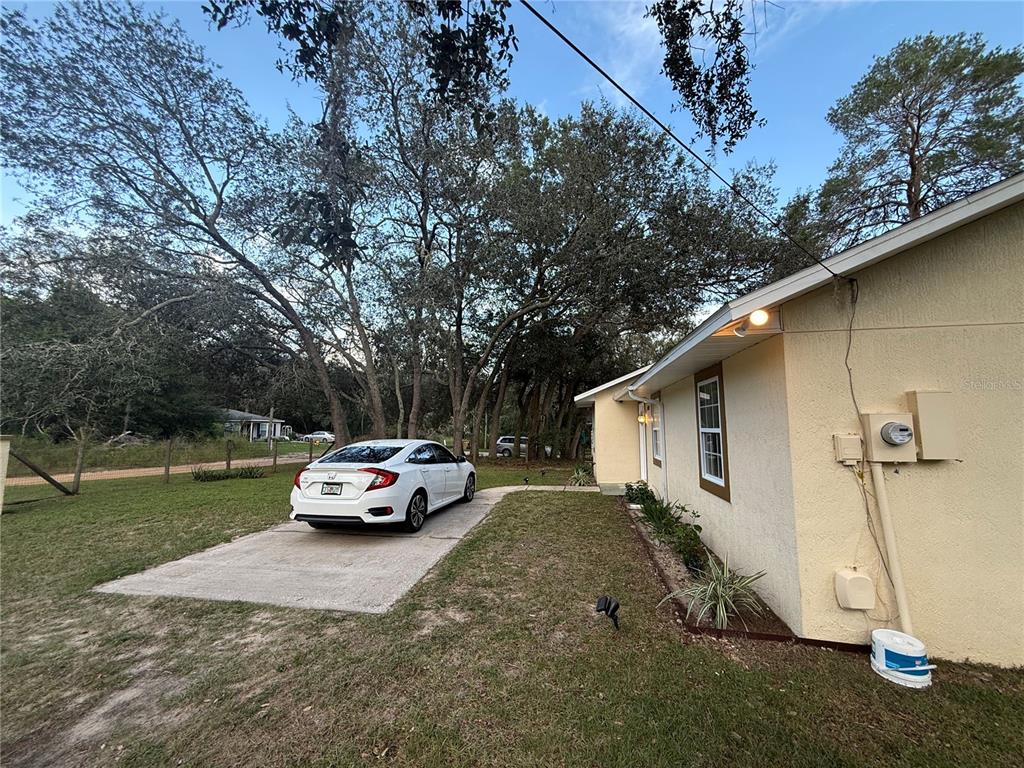 A white sedan is parked on a concrete driveway next to a yellow house — 40233 PALM STREET, LADY LAKE, FL