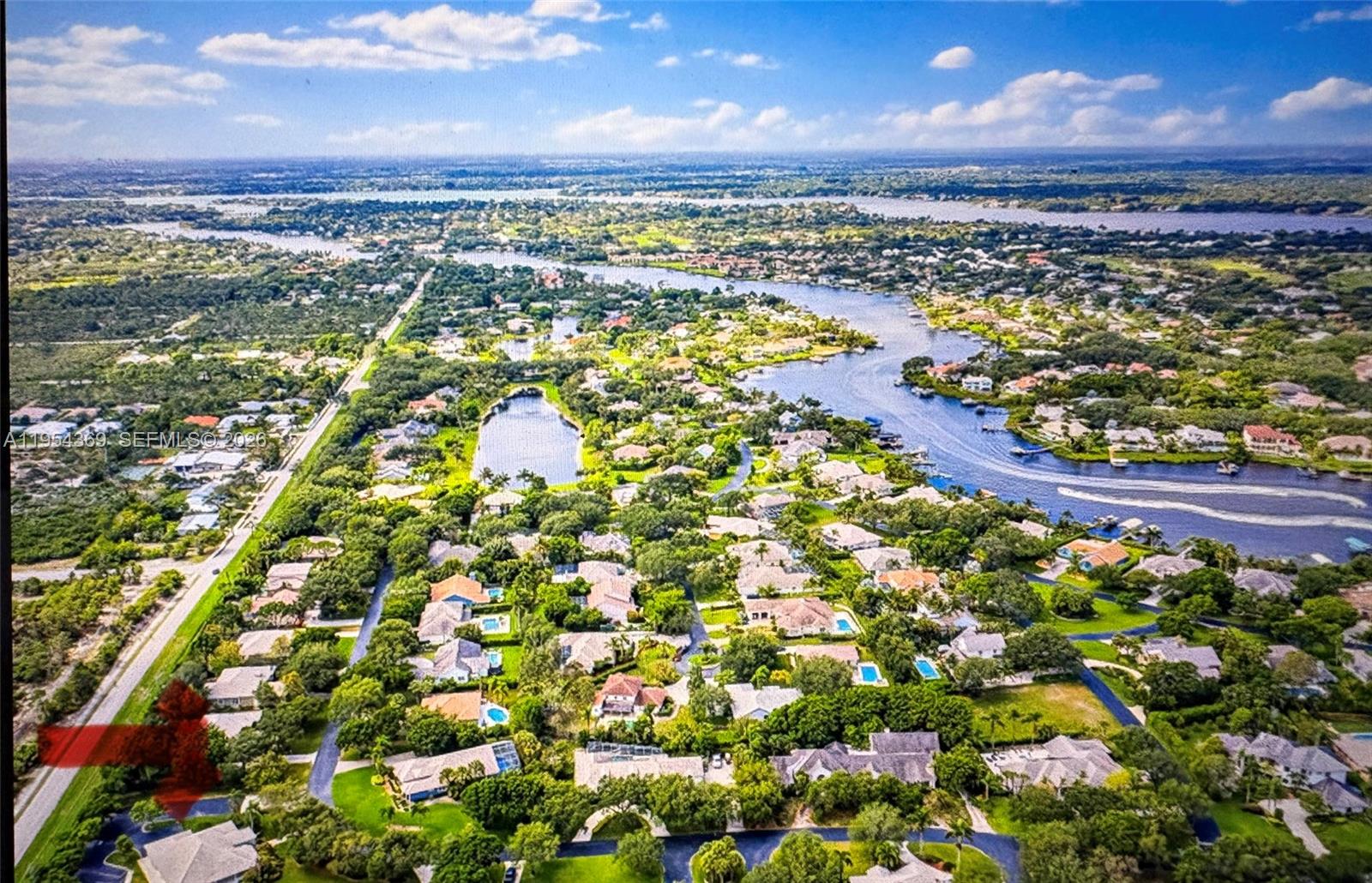 An aerial view shows a residential neighborhood with many houses, lush trees, and a waterway — 18265 SE Ridgeview Dr, Tequesta FL 33469, TEQUESTA, FL