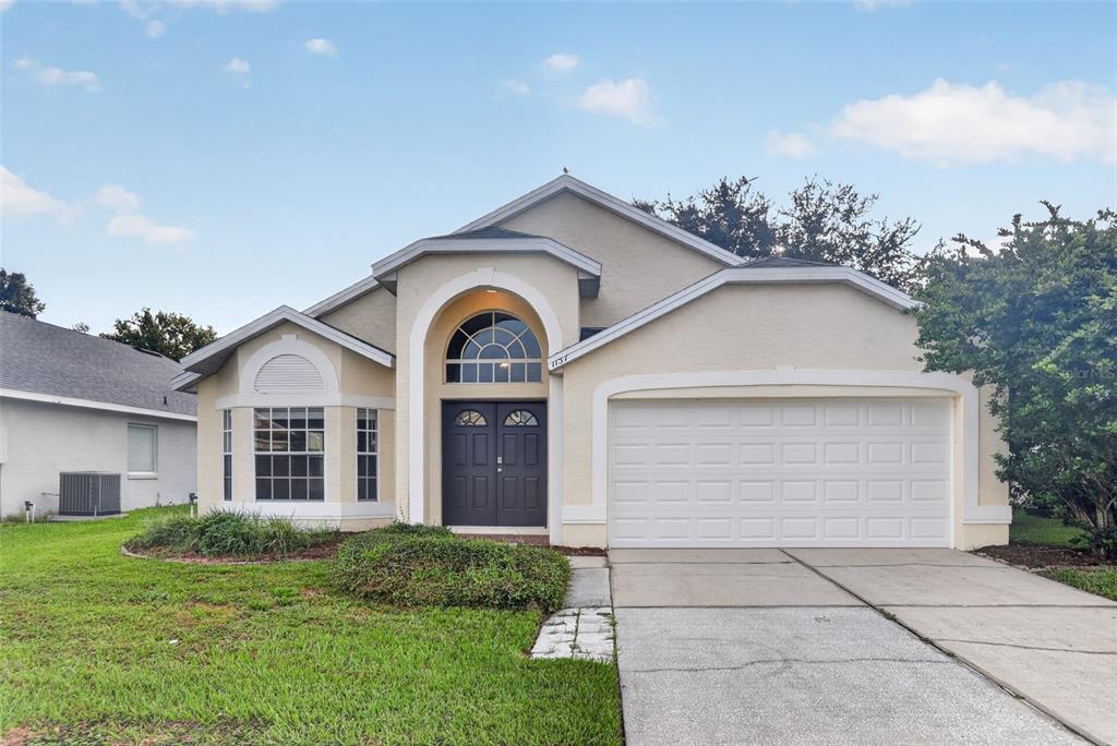 A single-story house with a beige stucco exterior, arched entryway, and a two-car garage — 1157 BALLYSHANNON PARKWAY, ORLANDO, FL