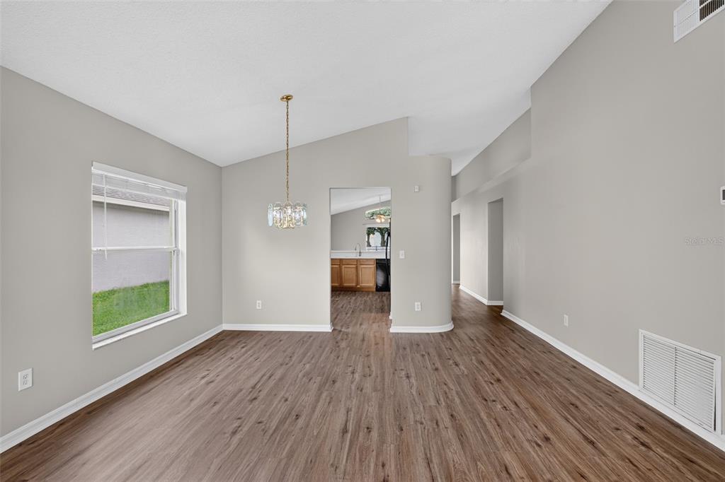 An empty dining room with wood-look flooring, a vaulted ceiling, and a view into the kitchen — 1157 BALLYSHANNON PARKWAY, ORLANDO, FL