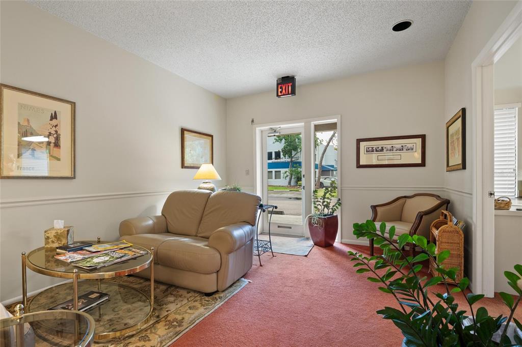 A waiting room features a tan loveseat, glass coffee table, carpeted floor, and an exit door — 2424 ENTERPRISE ROAD UNIT A, CLEARWATER, FL