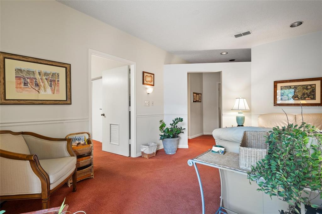 A living room features red carpeting, beige walls, a white door, and a potted plant — 2424 ENTERPRISE ROAD UNIT A, CLEARWATER, FL