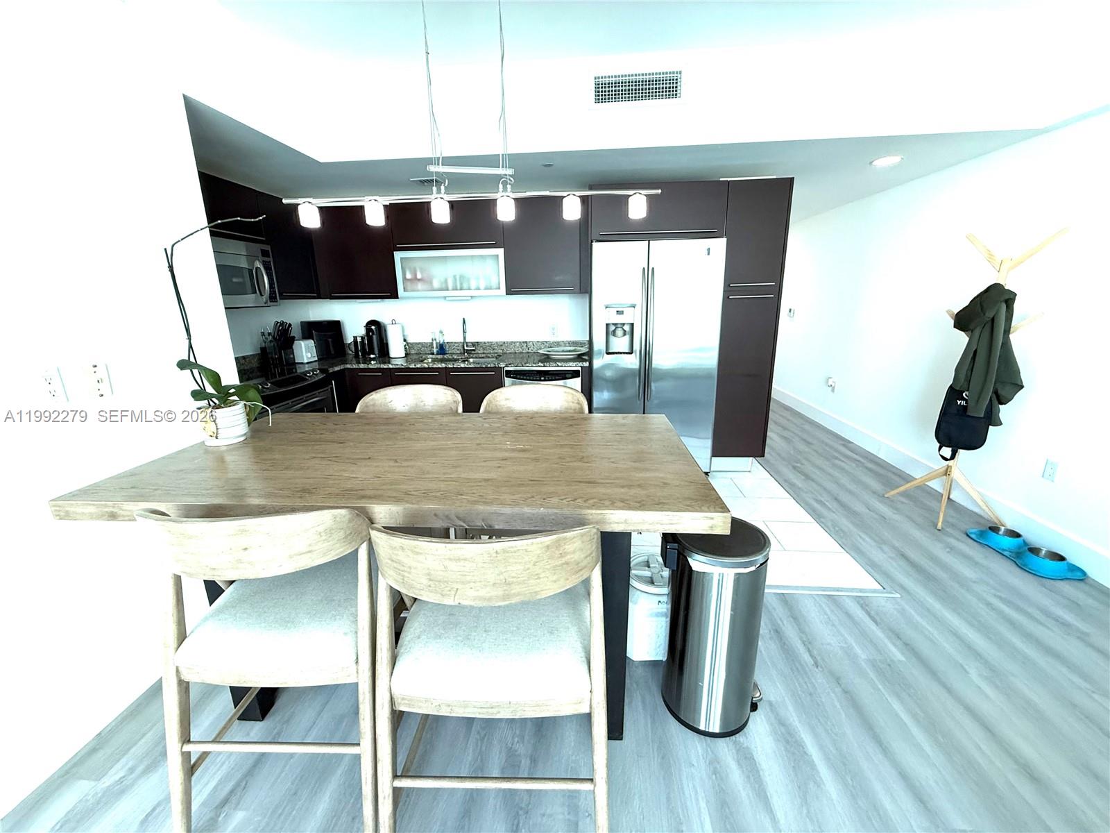 A kitchen features dark wood cabinetry, stainless steel appliances, and a wooden dining table — 950 Brickell Bay Dr # 2706, Miami FL 33131, MIAMI, FL