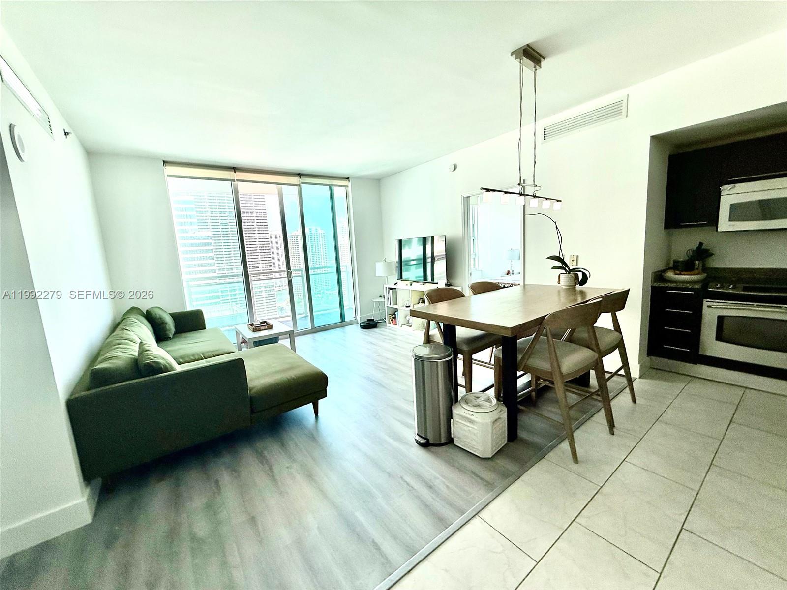 A modern living and dining area features a green sofa, wood table, and tile flooring — 950 Brickell Bay Dr # 2706, Miami FL 33131, MIAMI, FL