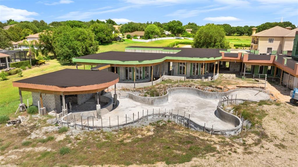 An aerial view shows a house under construction with a large, unfinished freeform swimming pool — 9621 WINDY RIDGE ROAD, WINDERMERE, FL