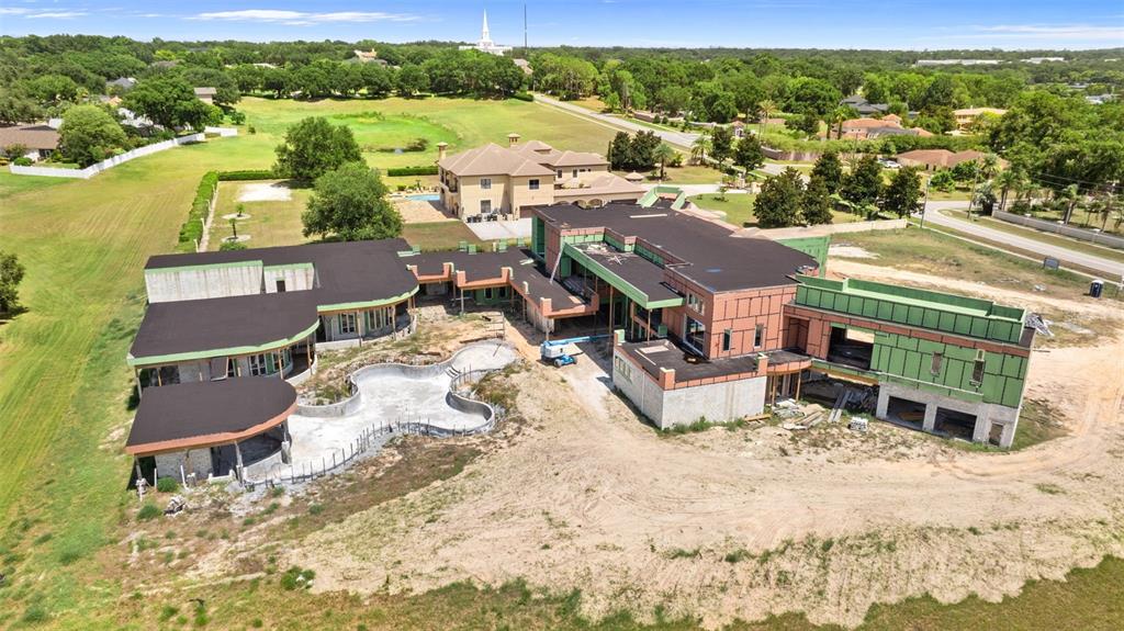 An aerial view shows a large, unfinished residential construction project with an outdoor swimming pool — 9621 WINDY RIDGE ROAD, WINDERMERE, FL
