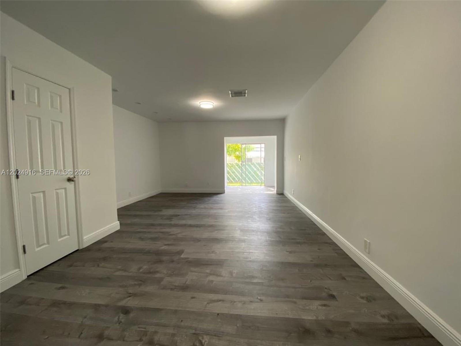 An empty room features gray wood-look flooring, white walls, and a sliding glass door — 2460 Taylor St # 1C, Hollywood FL 33020, HOLLYWOOD, FL