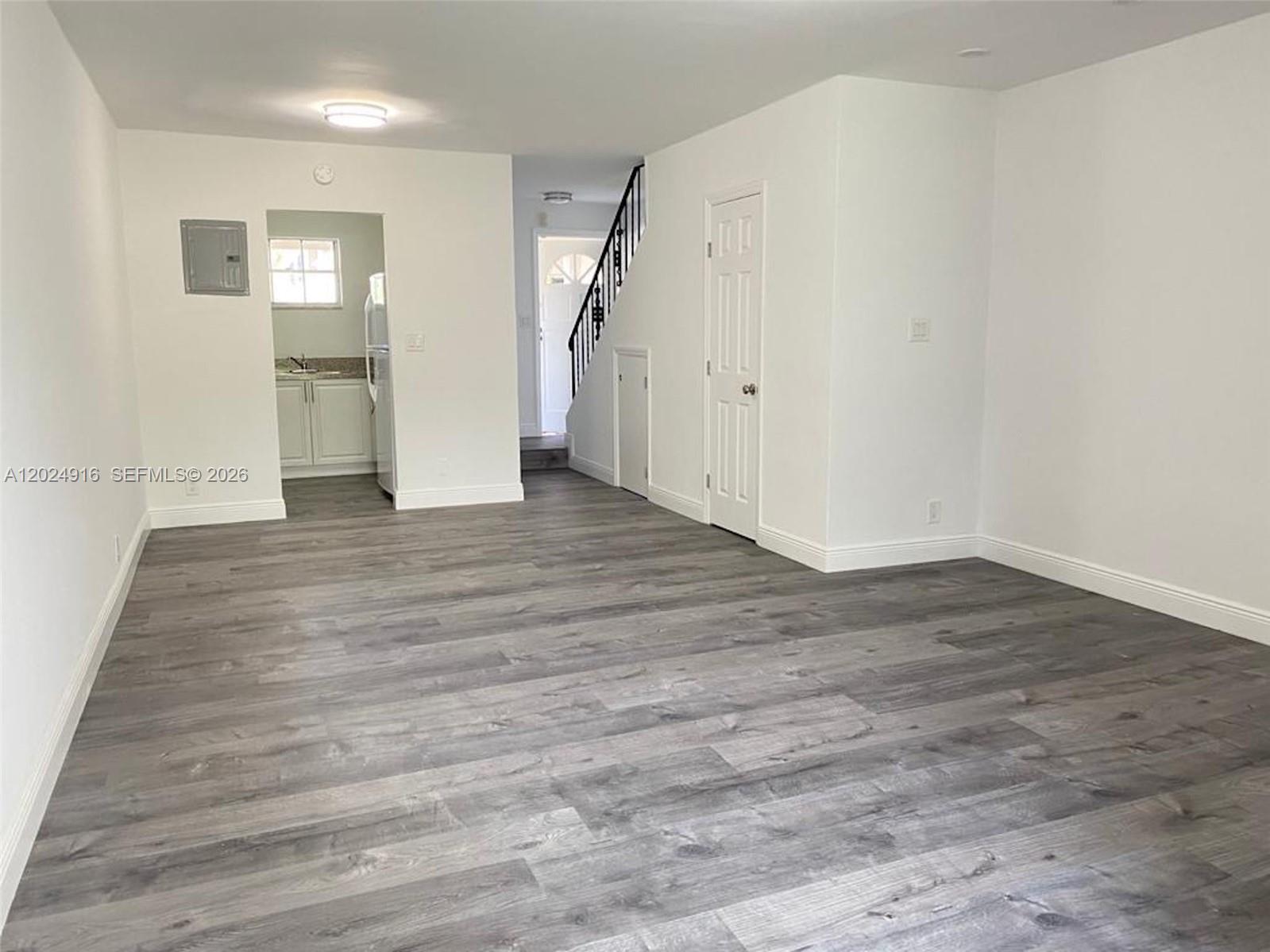 An interior view shows a living area with gray wood-look flooring and a small kitchen — 2460 Taylor St # 1C, Hollywood FL 33020, HOLLYWOOD, FL