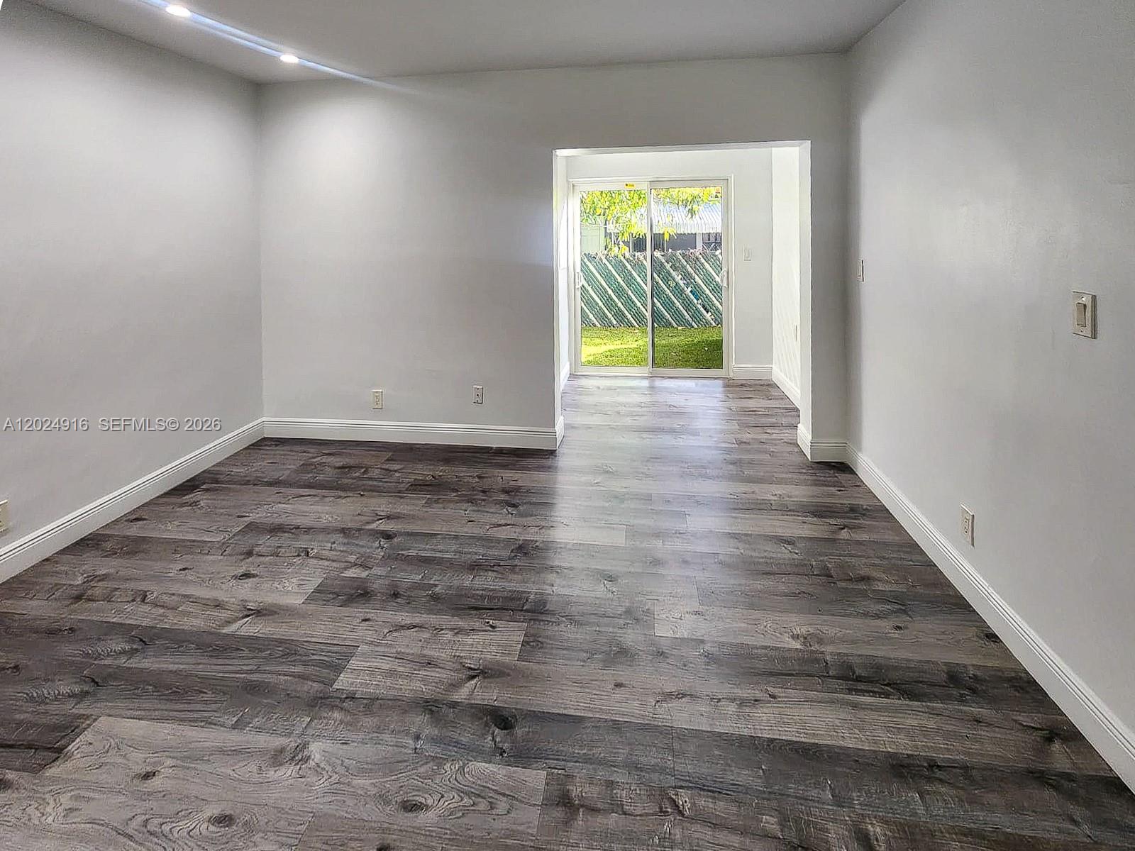 An empty room features gray wood-look flooring, white walls, and a sliding glass door — 2460 Taylor St # 1C, Hollywood FL 33020, HOLLYWOOD, FL