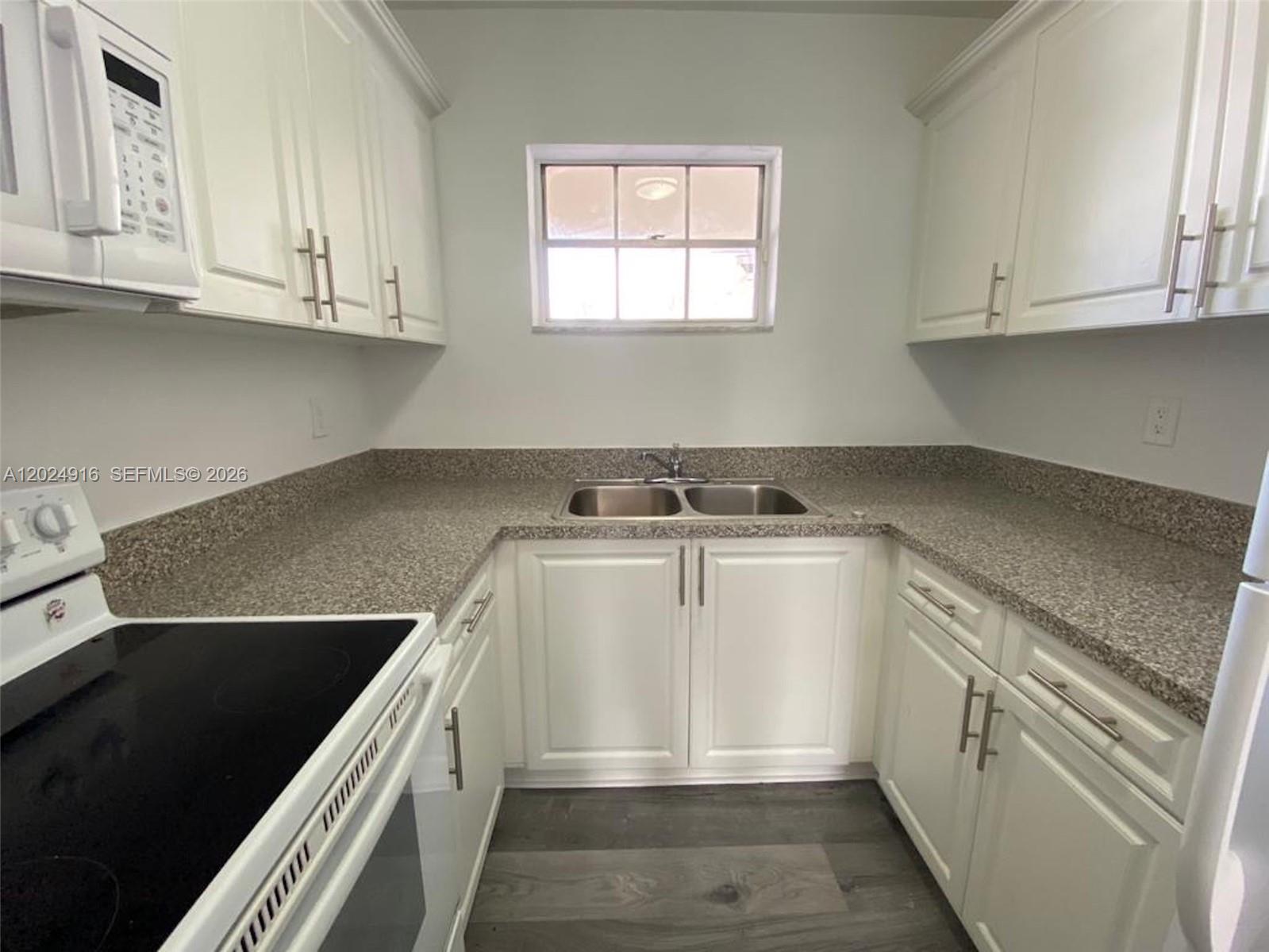 A small kitchen features white cabinets, granite countertops, and a stainless steel sink — 2460 Taylor St # 1C, Hollywood FL 33020, HOLLYWOOD, FL