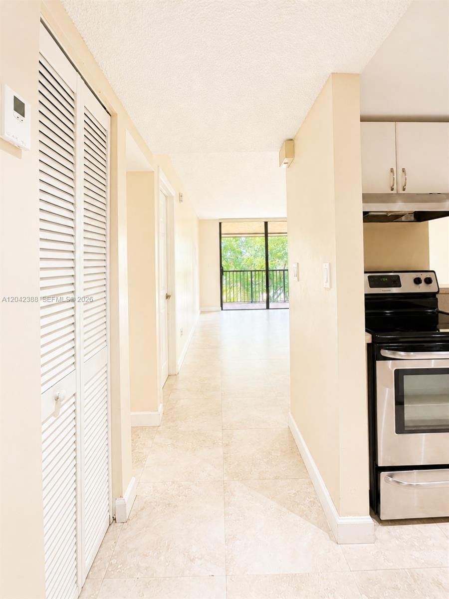 A hallway with tile flooring leads toward a balcony with a view of trees — 14421 N Kendall Dr # 000, Miami FL 33186, MIAMI, FL