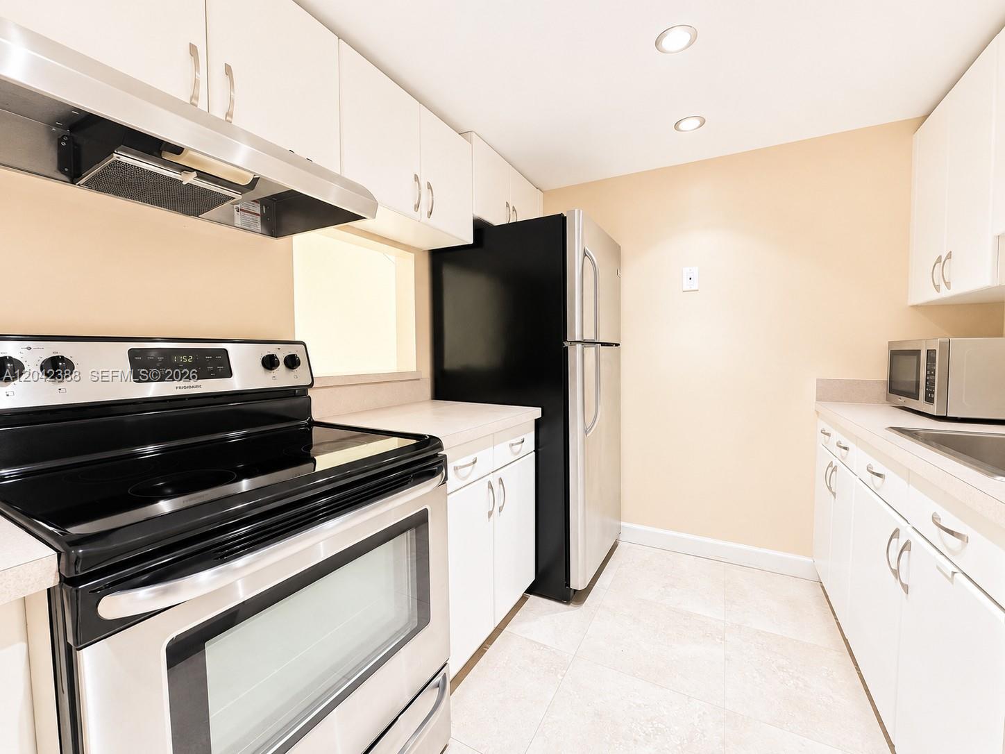 A galley kitchen features white cabinets, stainless steel appliances, and light-colored tile flooring — 14421 N Kendall Dr # 000, Miami FL 33186, MIAMI, FL