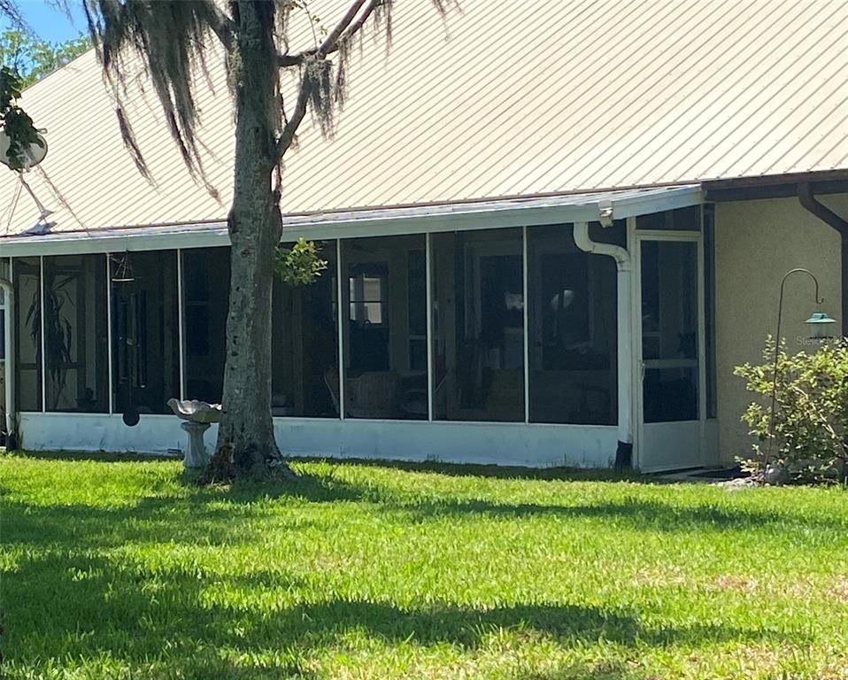A screened-in porch with a metal roof sits beside a tree on a grassy lawn — 229 LAKE IDA POINT DRIVE, INTERLACHEN, FL