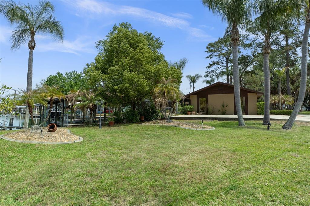 A grassy backyard features palm trees, a boat dock, and a small house with a patio — 239 SE PARADISE POINT ROAD, CRYSTAL RIVER, FL