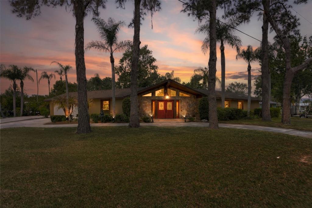 A single-story house with a stone facade and red double doors at sunset — 239 SE PARADISE POINT ROAD, CRYSTAL RIVER, FL