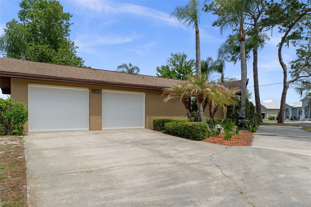 A tan house exterior features a two-car garage, a concrete driveway, and several palm trees — 239 SE PARADISE POINT ROAD, CRYSTAL RIVER, FL