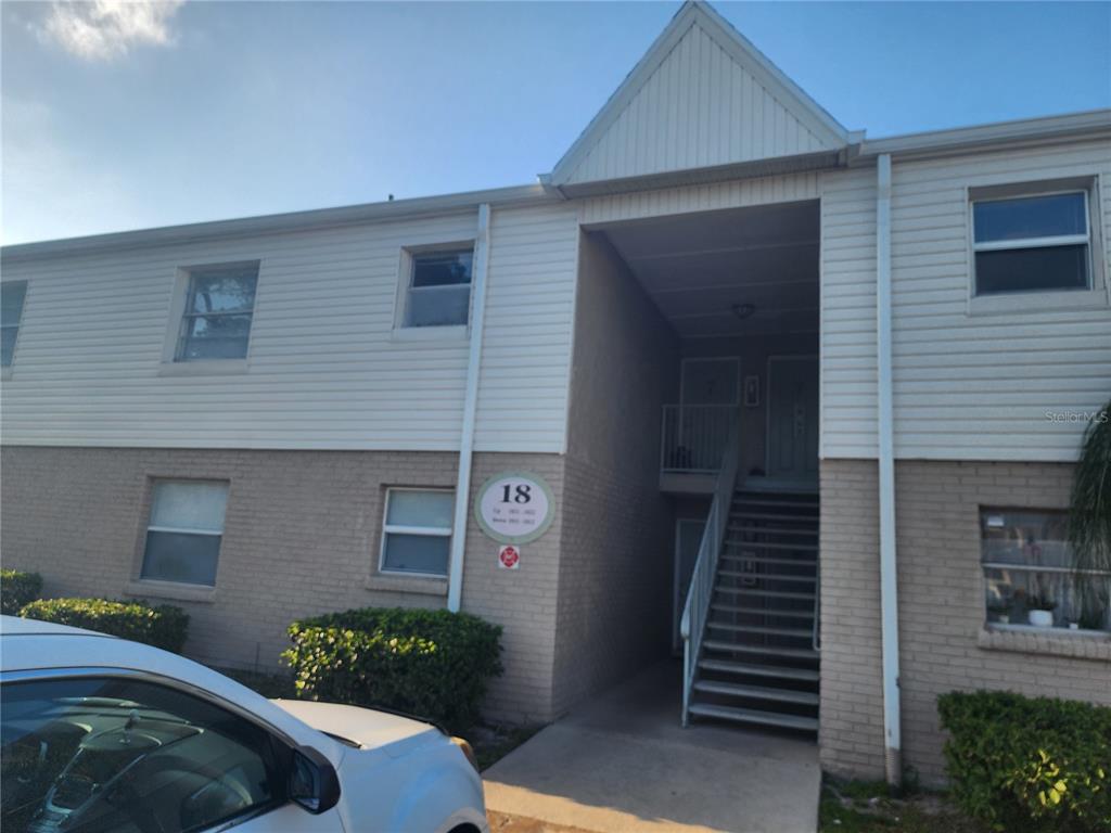 A two-story apartment building exterior features tan brick, white siding, and an outdoor staircase — 7210 N MANHATTAN AVENUE UNIT 1821, TAMPA, FL