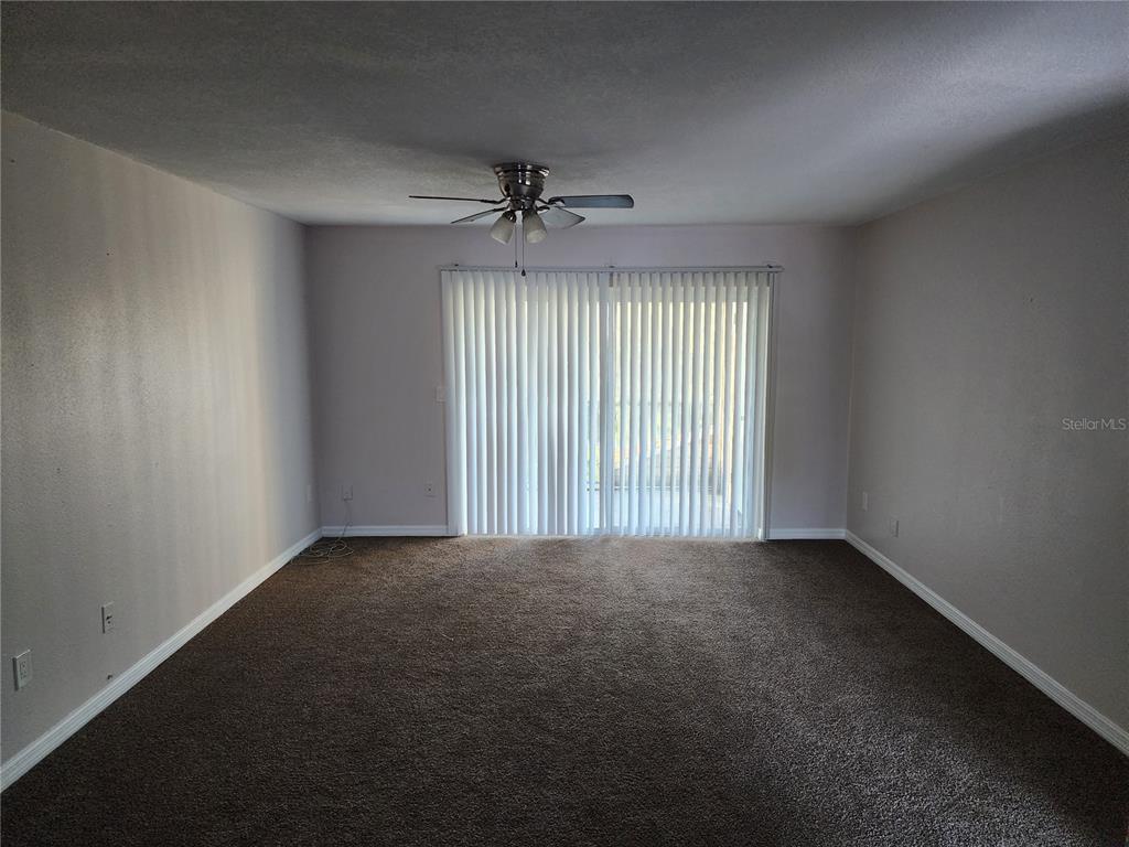 An empty room features brown carpeting, light-colored walls, a ceiling fan, and vertical window blinds — 7210 N MANHATTAN AVENUE UNIT 1821, TAMPA, FL